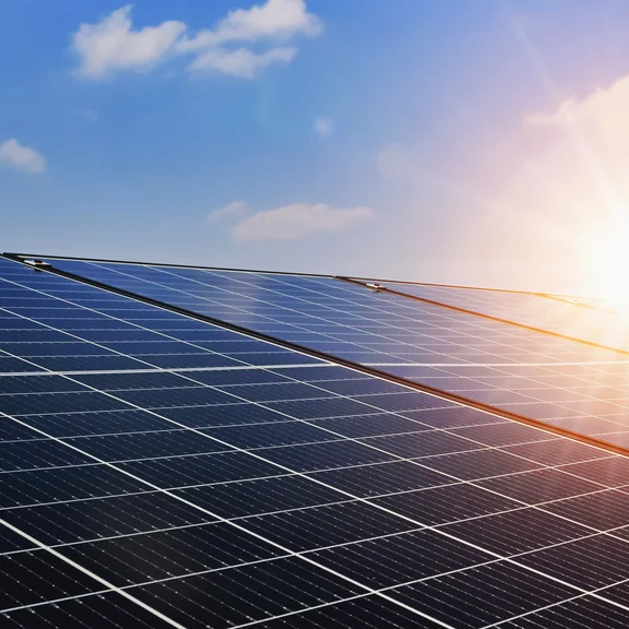 Solarmodule sind vor einem blauen Himmel mit Sonnenschein abgebildet.