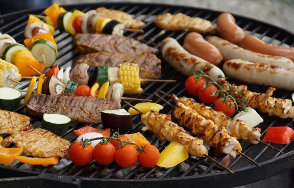 verschiedenes Gemüse, Bratwürste und Fleischspieße auf einem Holzkohle-Kugelgrill