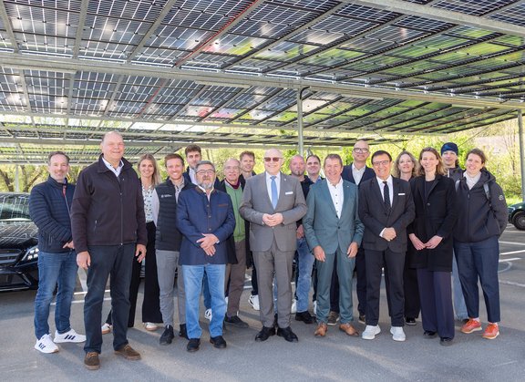 Gruppe von Mitarbeitenden und Projektbeteiligten steht unter einer überdachten Parkplatzanlage mit installierten Photovoltaikmodulen