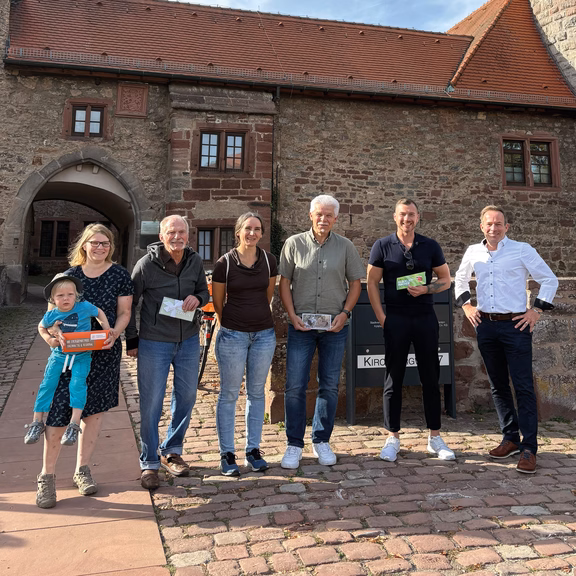Gewinner Großer Markt 2026 Im Mittelpunkt steht eine Gruppe von sechs Erwachsenen und einem Kind vor einem historischen Steingebäude. Mehrere Personen halten Karten bzw. Gutscheine; oben rechts ist das Logo „Stadtwerk Tauberfranken“ eingeblendet.