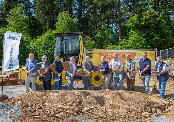 Gruppenfoto beim Spatenstich für das Projekt WaLuLiS: 10 Männer mit Schaufeln heben Erde vor einer Baumaschine. Im Hintergrund Banner mit der Aufschrift ‚Ihr Energiepartner – Stadtwerk Tauberfranken‘ sowie eine Fahne der Firma Anton Bokmeier GmbH. Die Veranstaltung findet bei sonnigem Wetter auf einer Baustelle vor einem Waldstück statt.