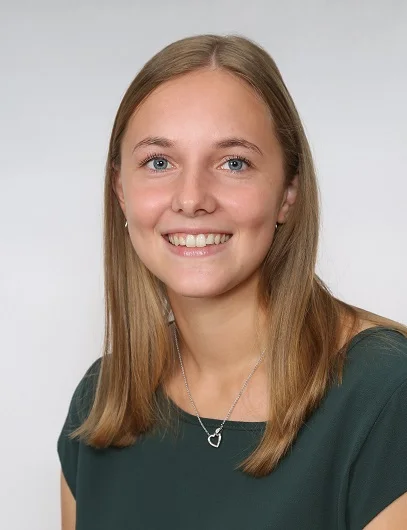 Rosa Appel Weibliche Person in grünem T-Shirt und langen braunbloden Haaren lächelt in die Kamera. Der Hintergrund ist weiß und der Bildausschnitt ist ein Portrait.