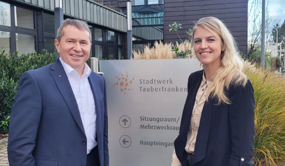 2 Personen stehen vor Eingangsschild mit Firmenbezeichnung des Stadtwerks
