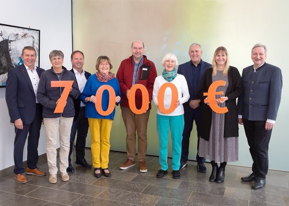 Die Zahl 7000 in großen orangenen Ziffern werden von verschiedenen Empäger*Innen der Spende gehalten