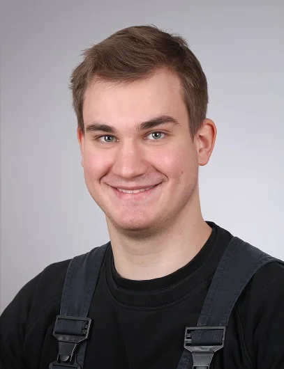 Tim Dankwardt Mitarbeiter in Arbeitsklamotten lächelt vor einem weißen Hintergrund in die Kamera.