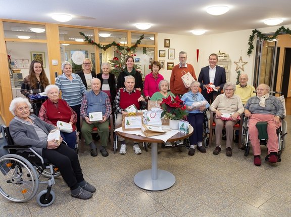 ältere Menschen im Rollstuhl sitzen hinter einem mit Weihnachtsgeschenken verpackten Tisch
