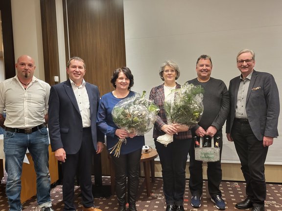 2 Mitarbeiterinnen mit Blumenstrauß und ein Mitarbeiter mit Bierpräsent werden von Geschäfstführern und Betriebsrat geehrt
