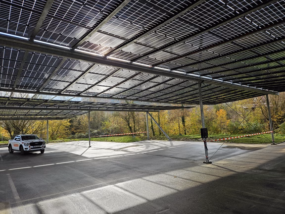 Parkplatz-PV-Anlage Ein Auto steht auf einer Parkplatzfläche, die mit PV-Modulen überdacht ist. Die Sonne scheint durch die Paneele und es ist ein freundlicher Wintertag.
