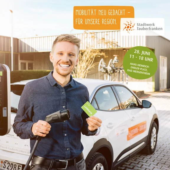 Person lädt ein Elektroauto an einer Ladesäule und hält eine Ladekarte; daneben Hinweis auf den Regionaltag am 28. Juni (11–18 Uhr) am Hans-Heinrich-Erler-Platz in Bad Mergentheim mit Fokus auf nachhaltige Mobilität