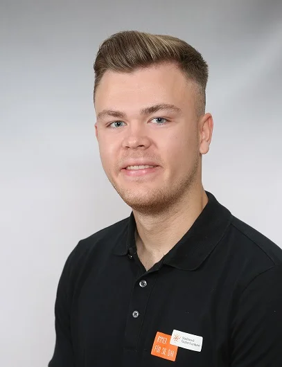 Julian Bullmann Mann in schwarzem Polo mit Stadtwerk-Logo lächelt in die Kamera. Er hat kurze dunkelblonde Haare und der Ausschnitt ist ein Portrait vor einer weißen Wand.