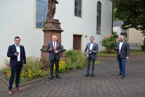 4 Personen mit Handy in der Hand vor Gebäude
