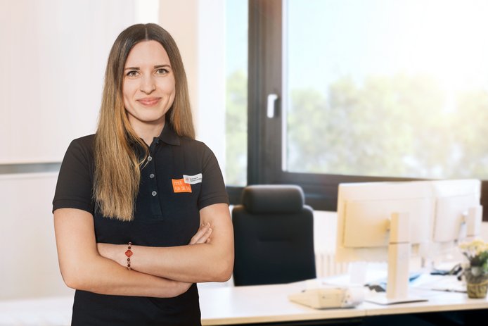 Eine Mitarbeiterin im schwarzen T-Shirt mit Stadtwerk-Logo steht in einem Büroraum. Die Arme sind verschränkt und sie lächelt in die Kamera. Ihre Haare sind lang, glatt und braun. 