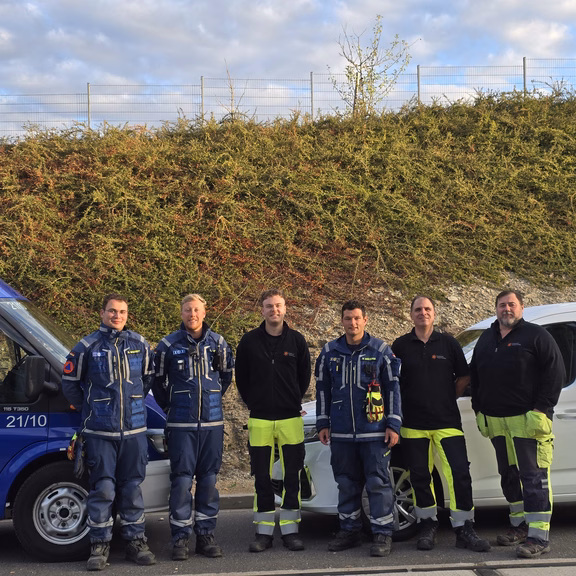 Sechs Personen in Einsatz- und Arbeitskleidung vor einem THW-Fahrzeug und einem weißen Firmenfahrzeug.