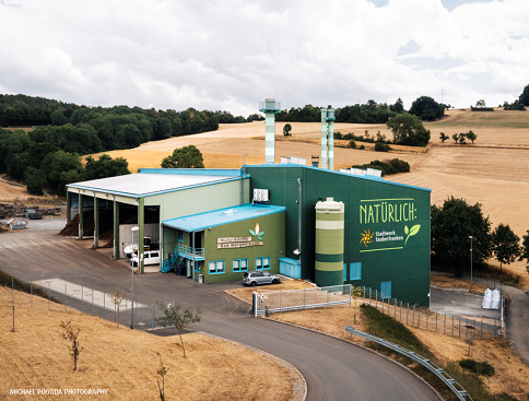 Blick auf das grüne Naturwärmkraftwerk mit Kaminen umgeben von Feldern im Sommer